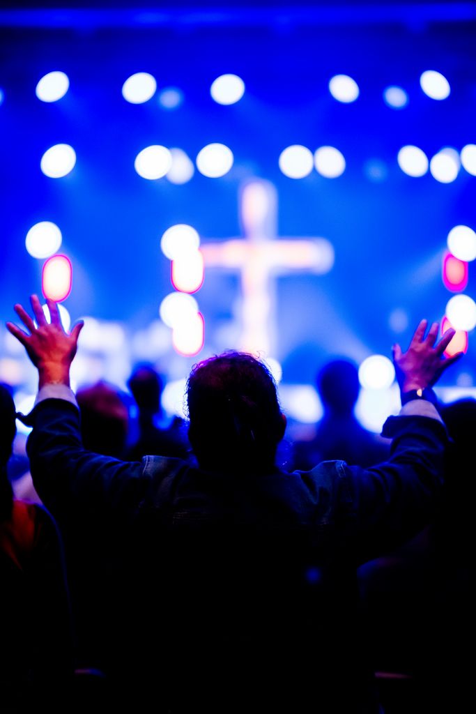 Silhouette of a person raising hands in worship during a vibrant church service with a cross in the background.